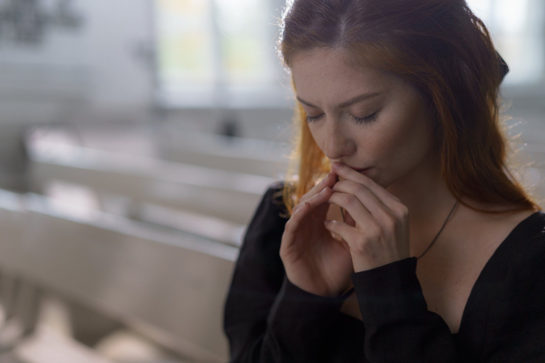 a woman in black long sleeves praying with her eyes closed